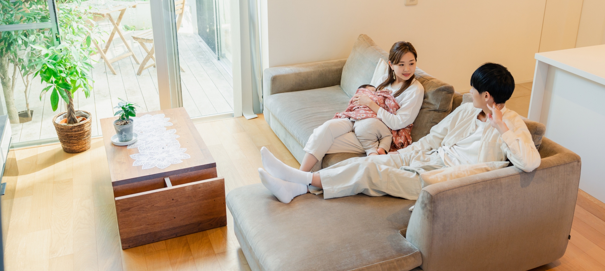 寝てる小さなこどもをだっこしてソファで会話を楽しむ若い夫婦